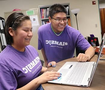 Two students looking at laptop and smiling